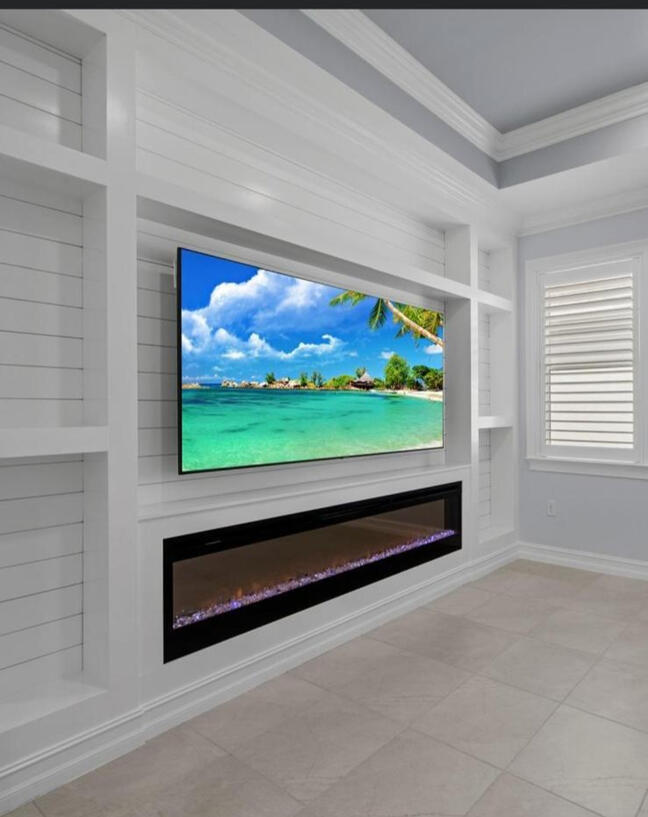 Custom Entertainment Wall – Seamless Function & Style This striking built-in unit combines clean shiplap paneling, integrated shelving, and a modern electric fireplace beneath a wall-mounted TV. Finished in crisp white with elegant crown molding, the desig